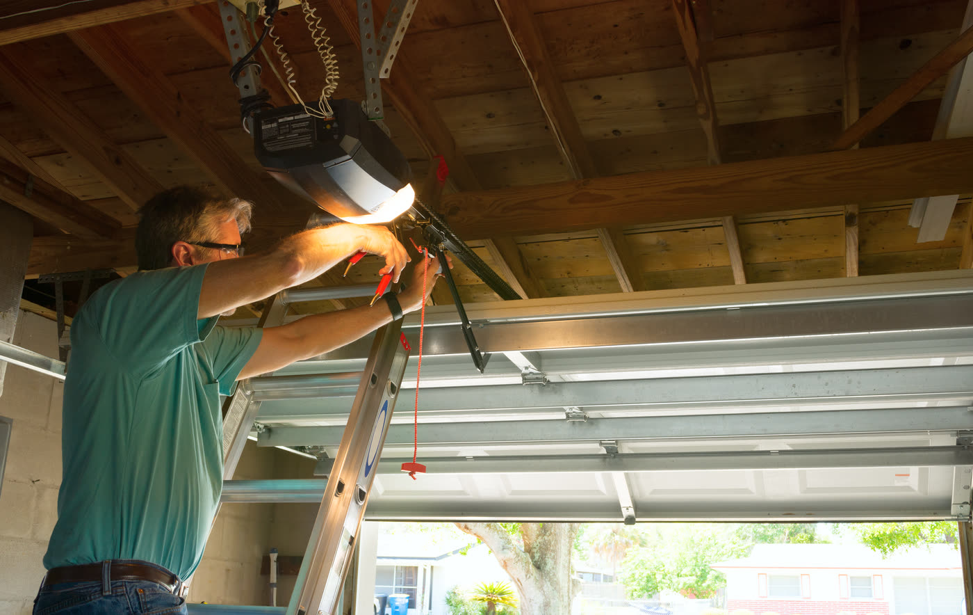 A technician on a ladder servicing a garage door opener