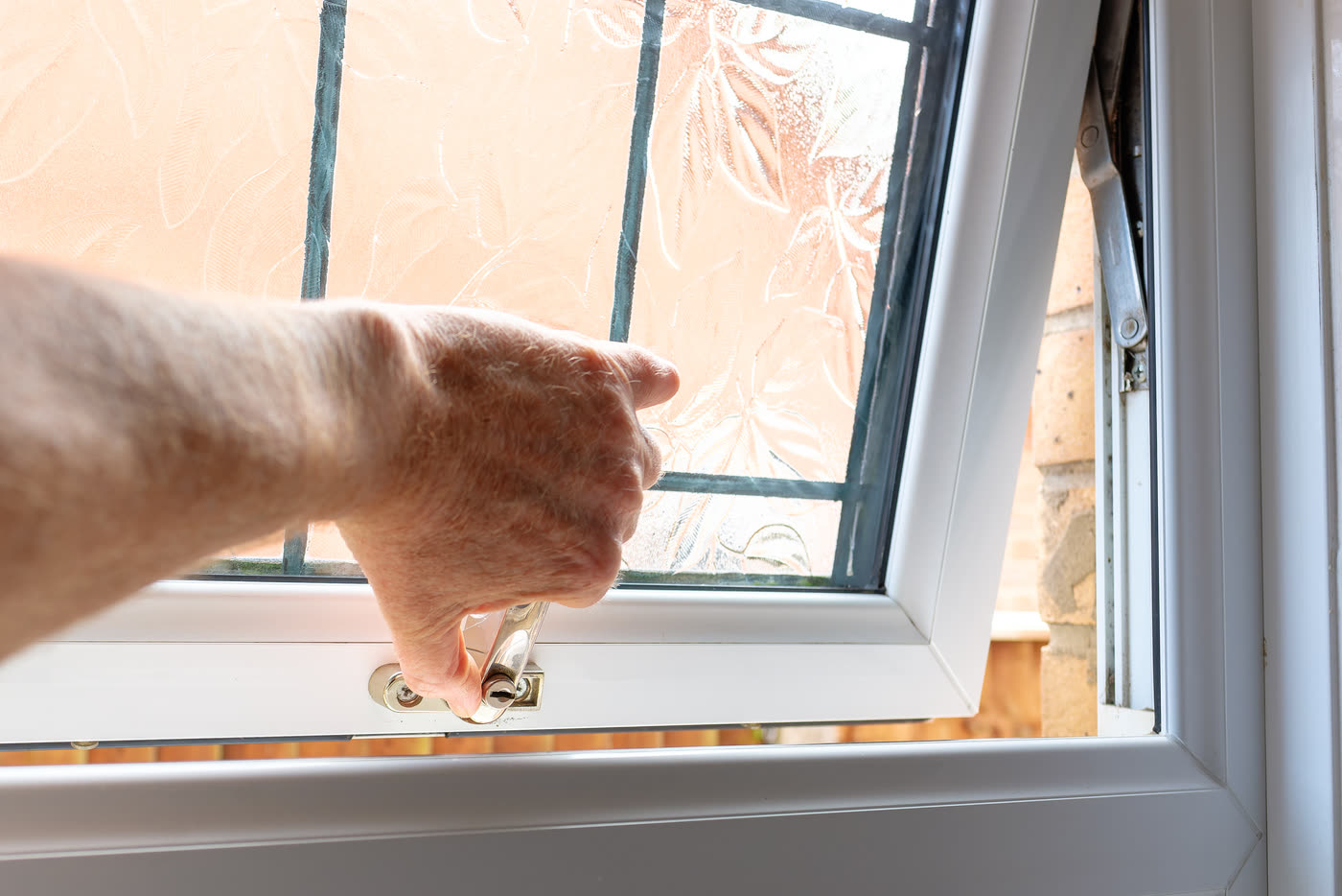 A hand turning the crank handle of a casement window pushed open