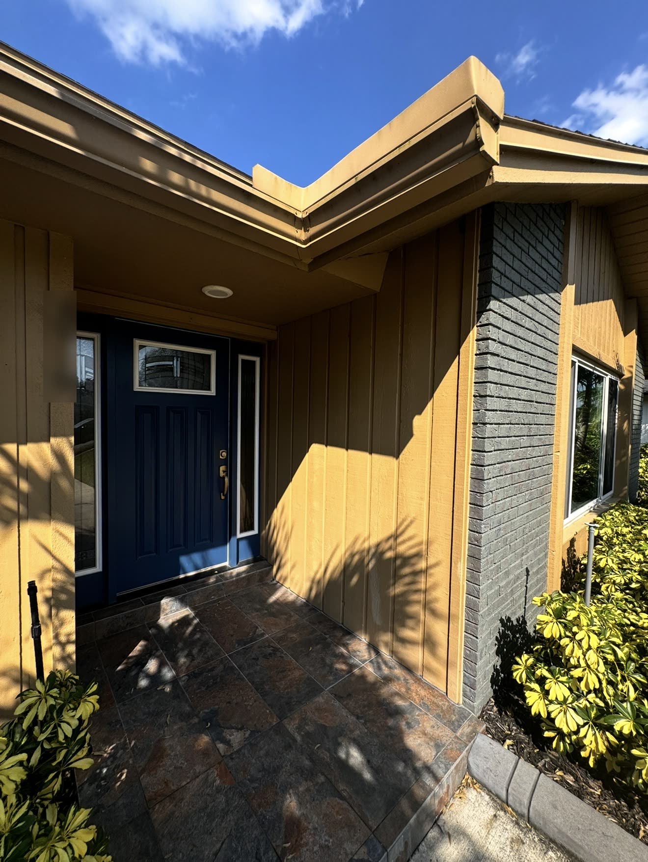 A navy entry door with a sidelight and a glazed upper panel under a covered entry