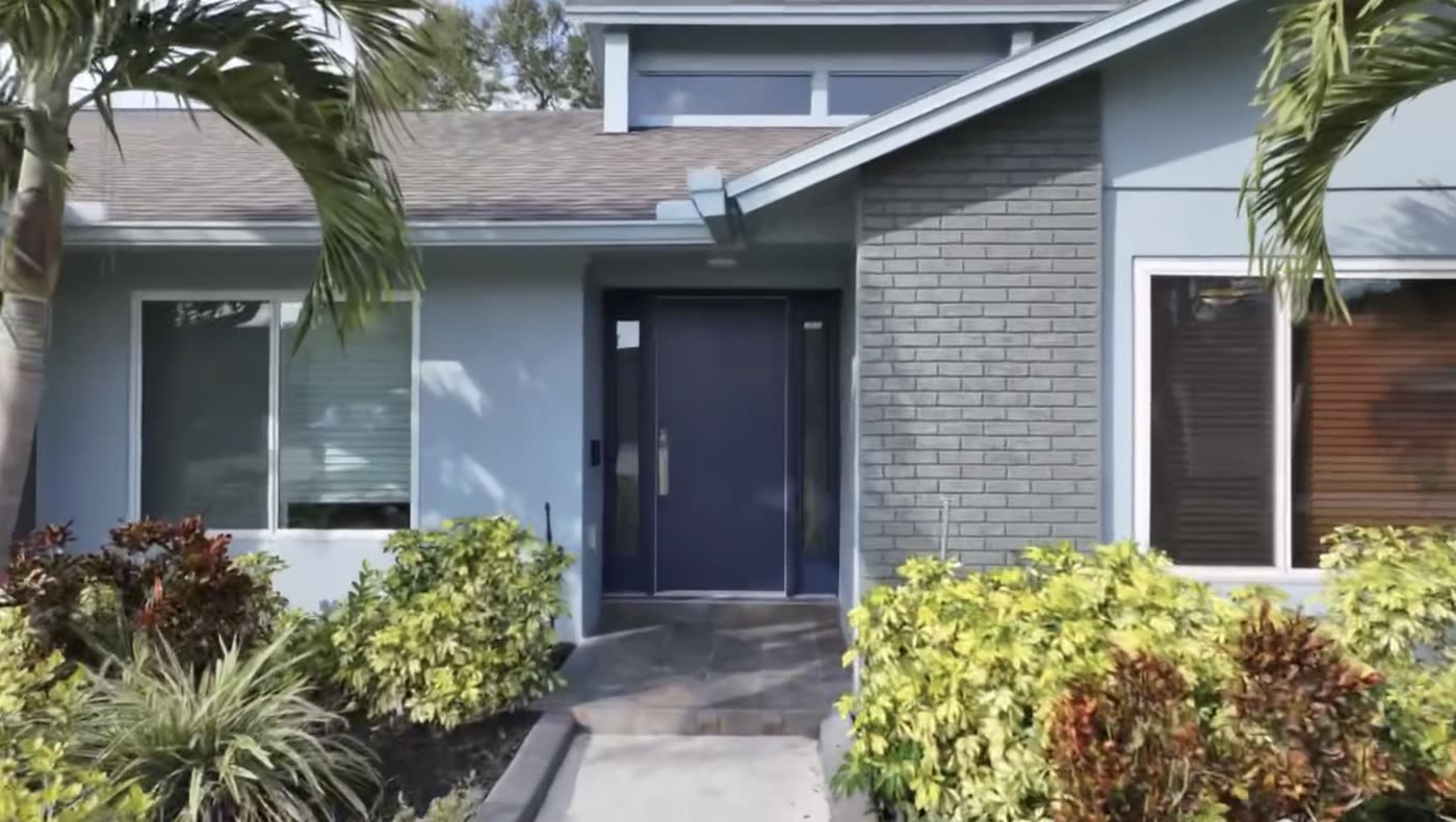 A navy entry door with sidelight and transom on a repainted grey-blue house