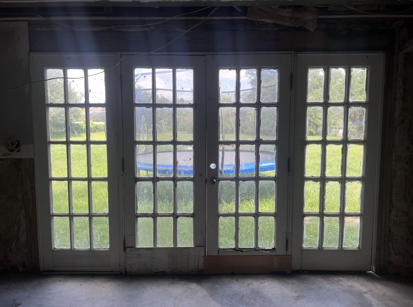 The original French doors in a stripped room, glass clouded and the sill rotted