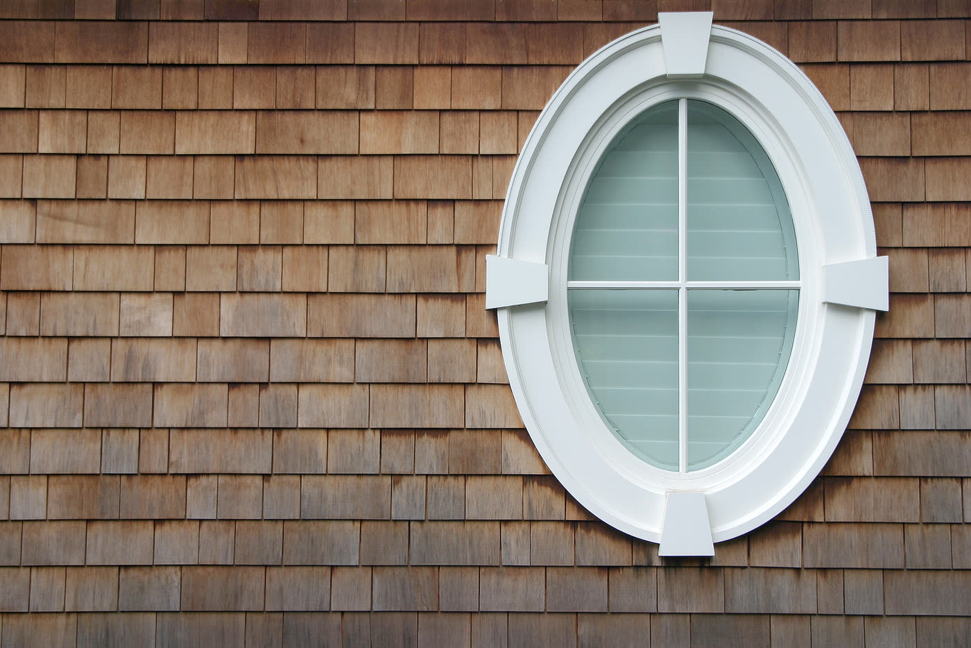 An oval fixed window with divided lights, set into cedar shingle siding