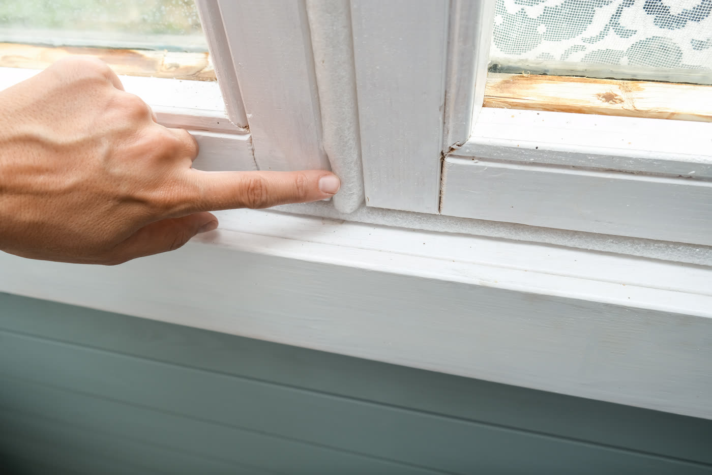 A finger pressing on worn weatherstripping in a window frame